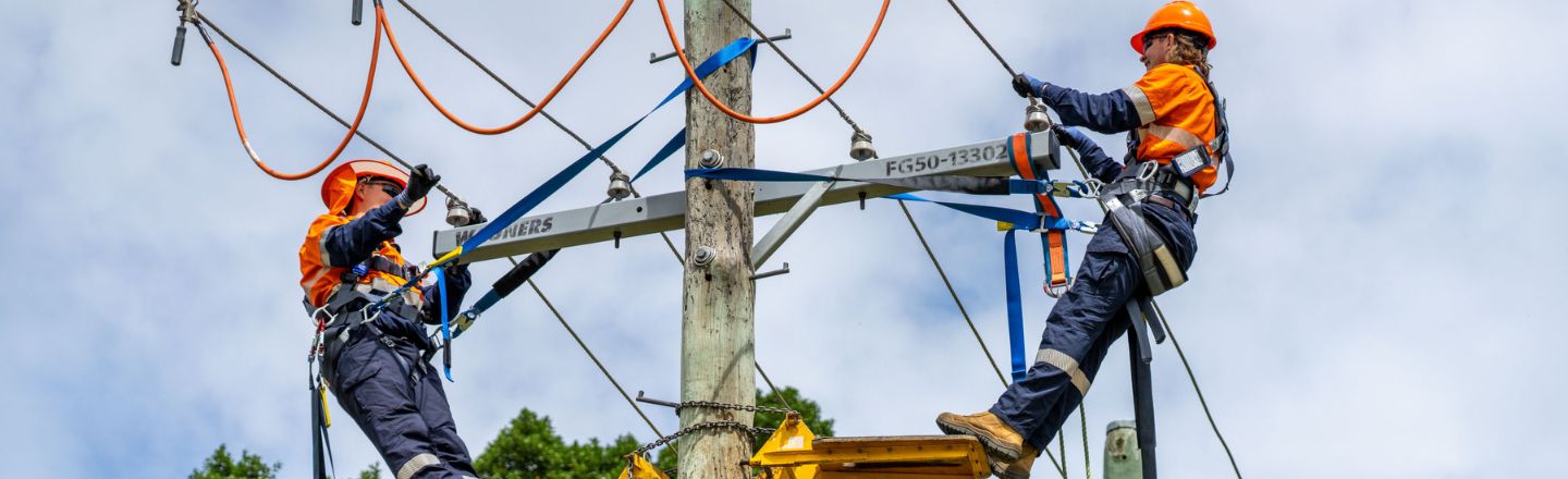 Two powerline workers repairing wires up a pole