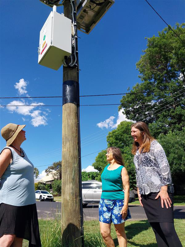3 people standing near a pole-mounted battery