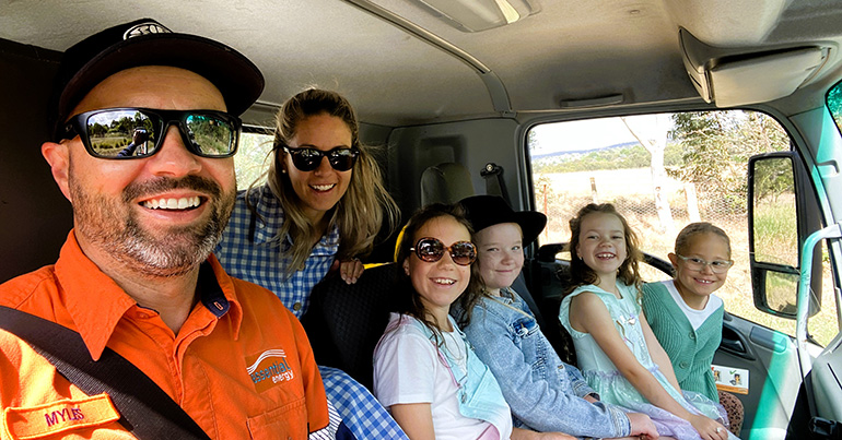 Two adults and four kids sitting in a truck smiling
