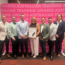 Seven people standing in front of a pink banner holding an award