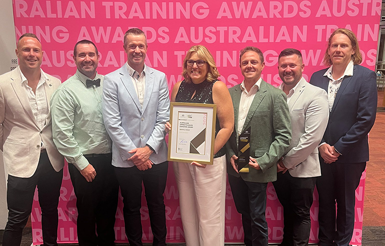 Seven people standing in front of a pink banner holding an award