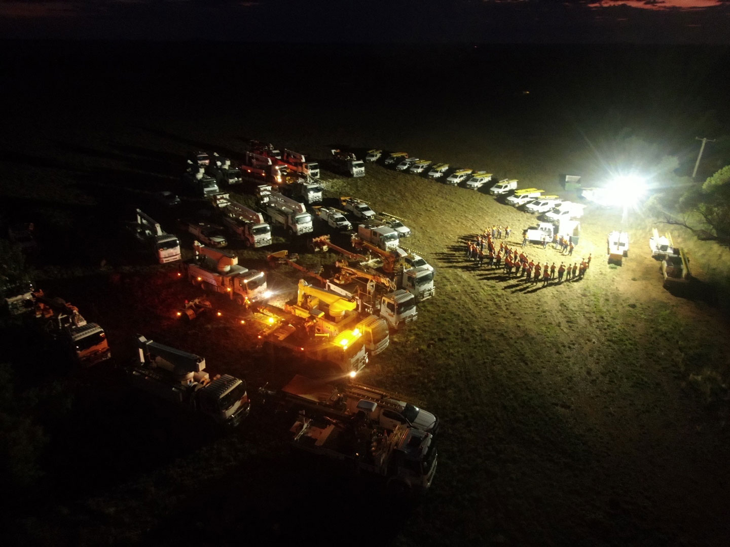 Congregation of workers and trucks at night planning maintenance effort.